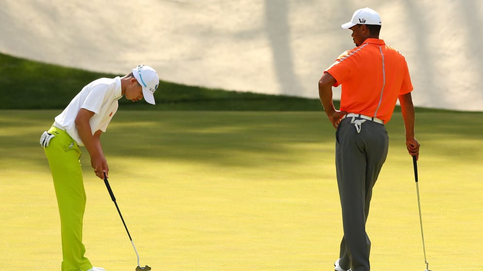 Guan Tianlang putts as Tiger Woods looks on 