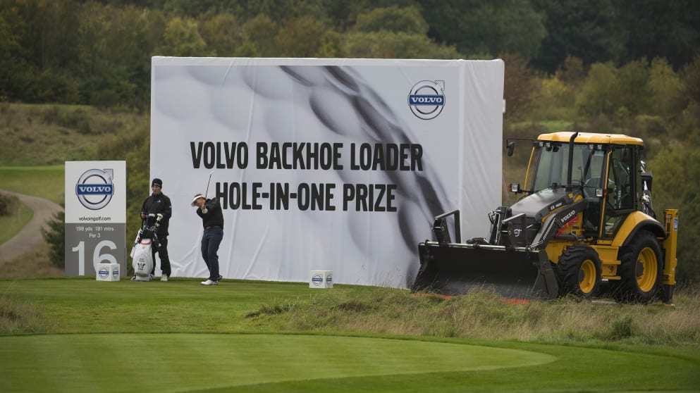 Joost Luiten teeing off next to one of this week's hole-in-one prizes, the Volvo BL71B Backhoe Loader 