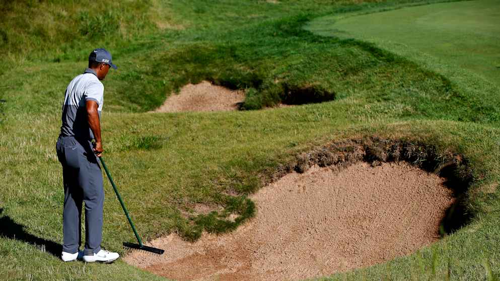 Tiger Woods rakes a bunker